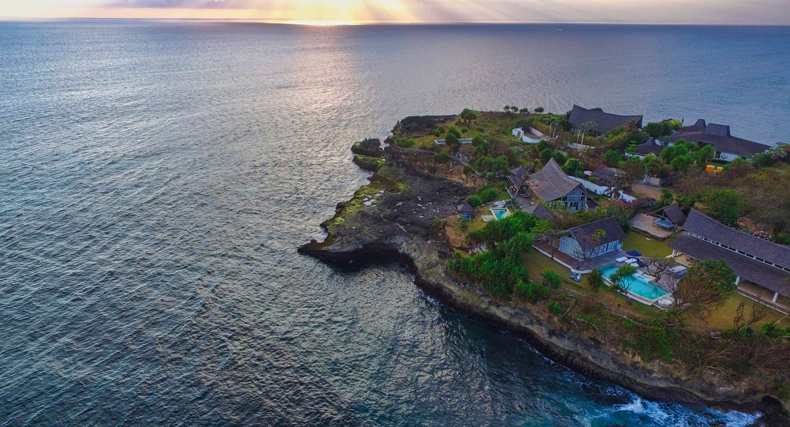 Aerial view of a rocky headland surrounded by ocean at sunset